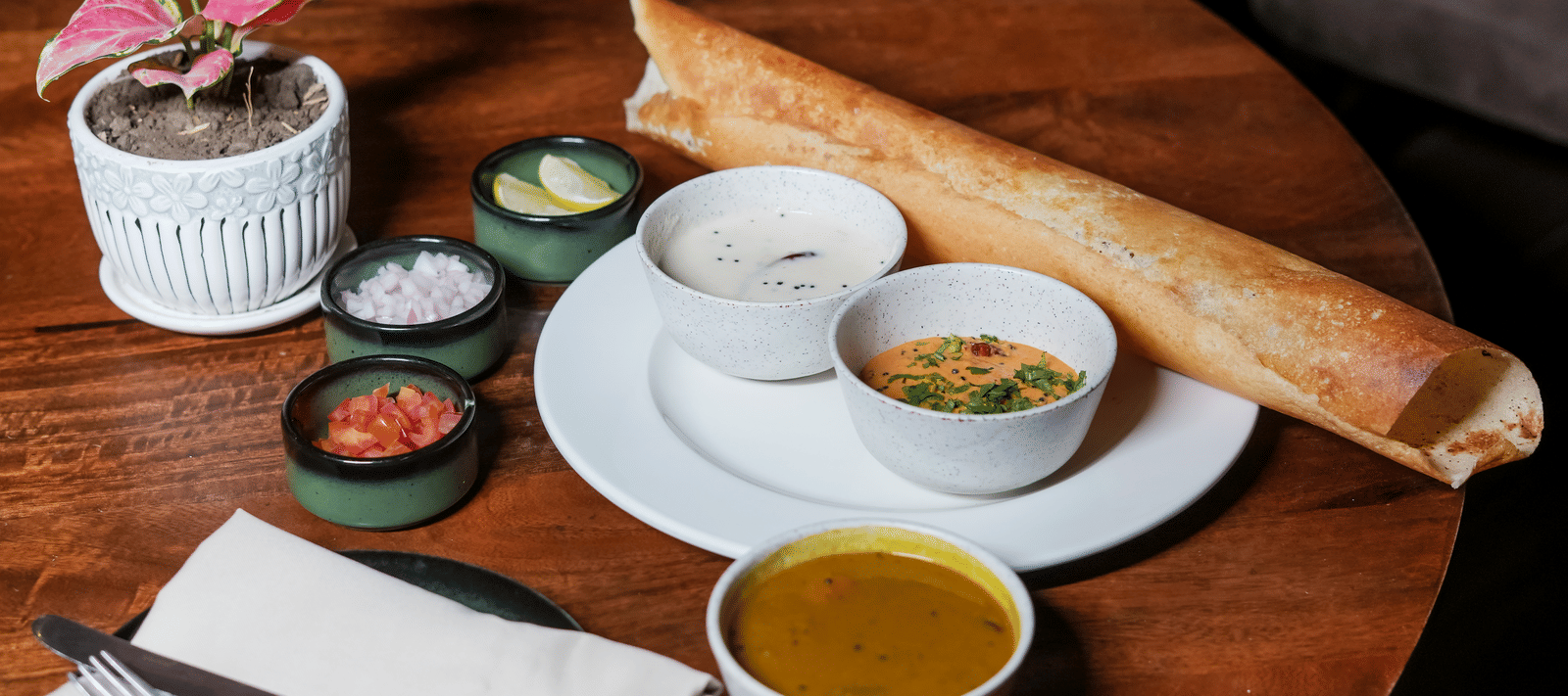A crisp, rolled dosa served on a wooden table with sambar, chutney, and other small side dishes at BluSalzz Select City Centre, Amritsar.