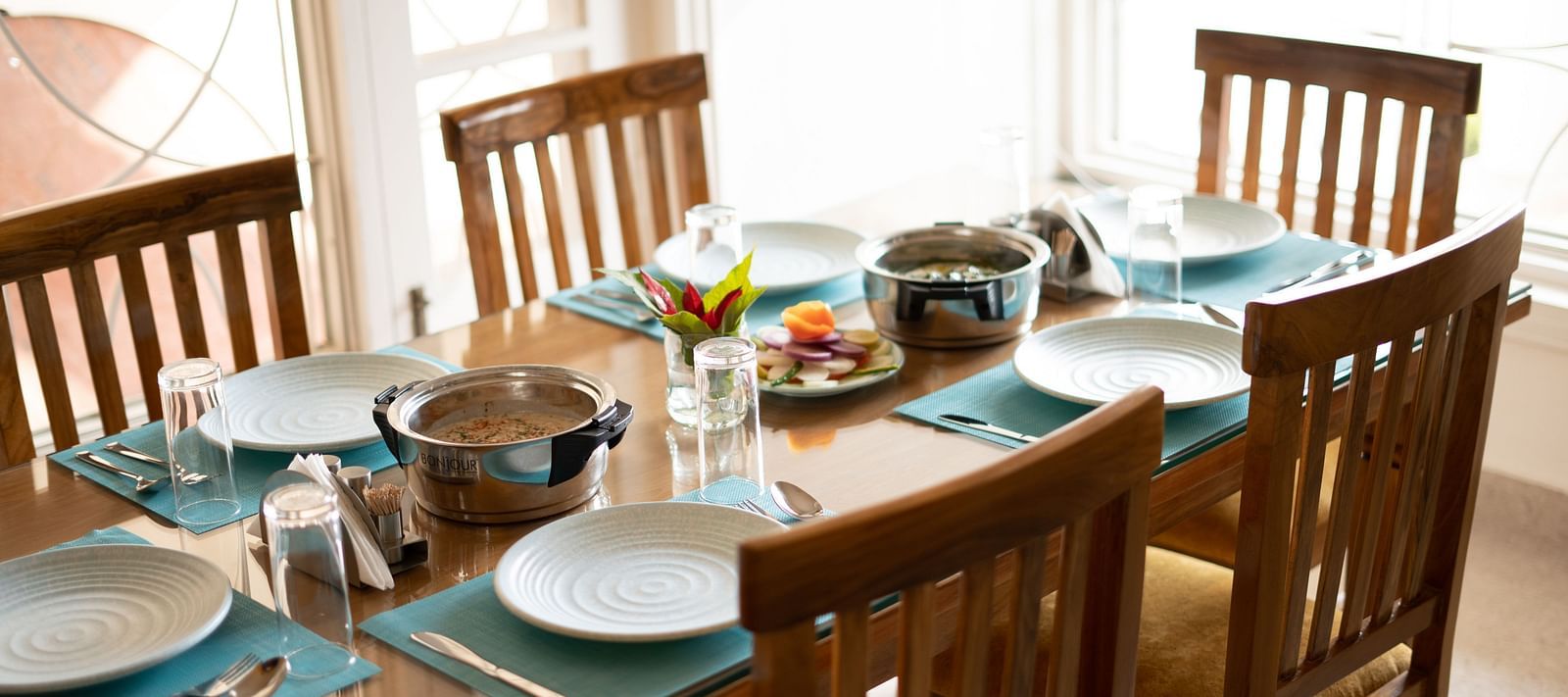 A dining table set with plates, glasses, and food in the middle, surrounded by chairs at BluSalzz Villas - The Green Roof, Bhimtal.