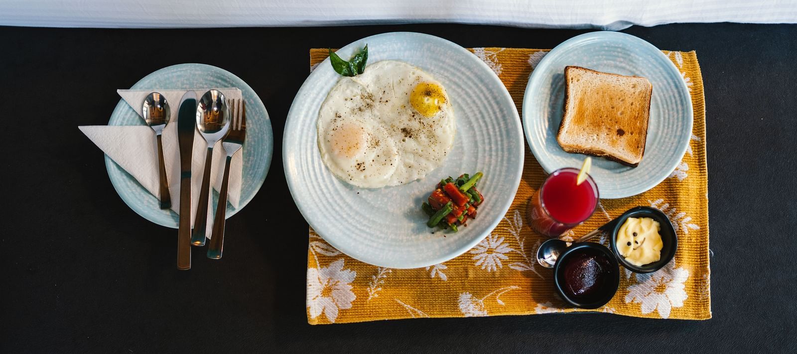 A top view of three plates at BluSalzz Villas - The Green Roof, Bhimtal, featuring toast, an omelette with vegetables, and cutlery alongside jam, butter, and a lit candle.
