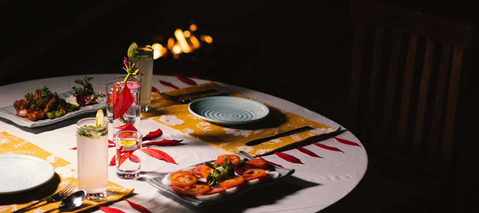 A fully set dinner table at BluSalzz Villas - The Green Roof, Bhimtal, with a cosy campfire glowing in the background.