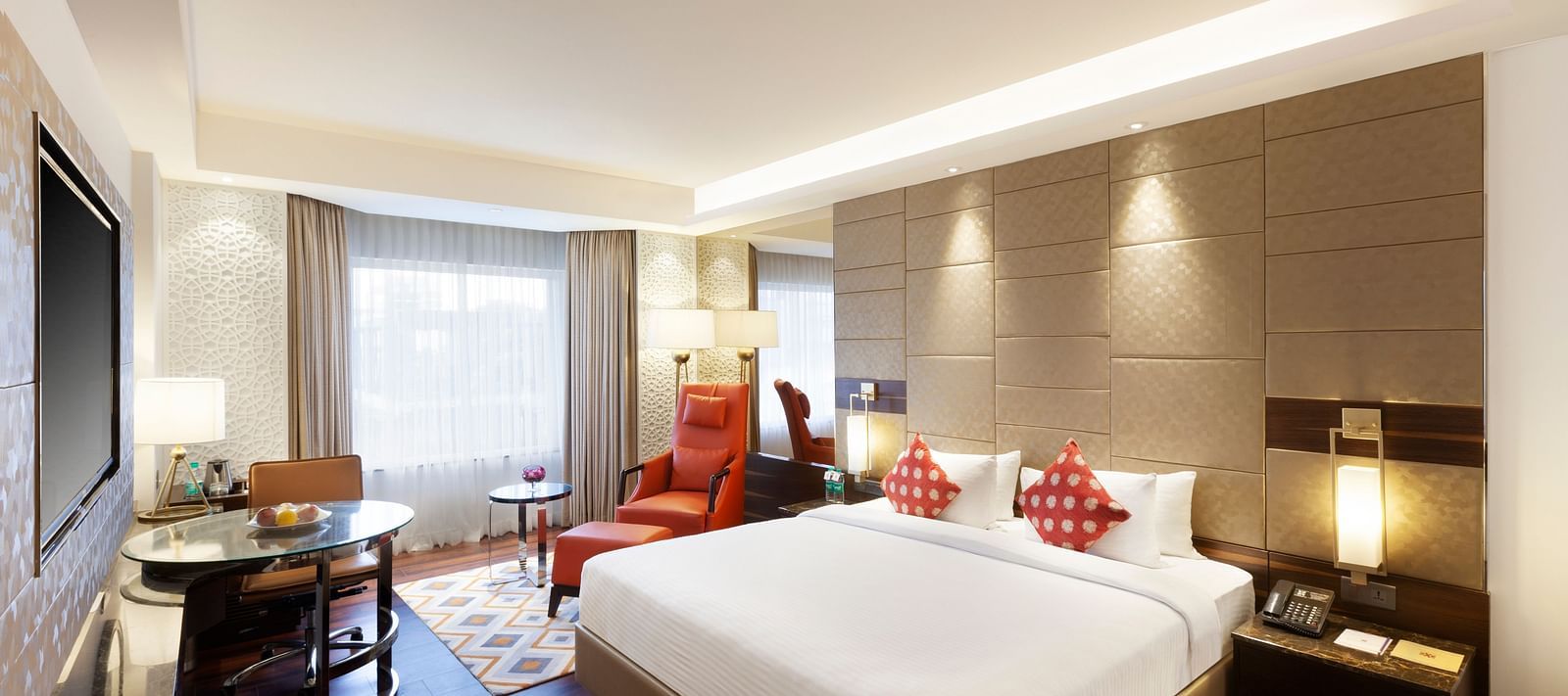 A spacious room with a large bed, wall-mounted TV, table, and cushioned chair, with curtains pulled to the side of the windows | Cenneys Gateway
