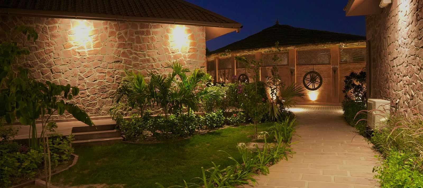 A pathway lit with lights and grass on both sides at Surpura Bagh.