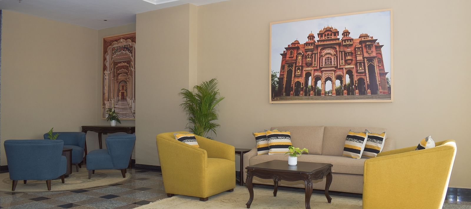 A hotel lobby with a beige sofa, yellow and blue armchairs, a coffee table, and a large framed image of an Indian palace - Urban Suites by BluSalzz, Jaipur