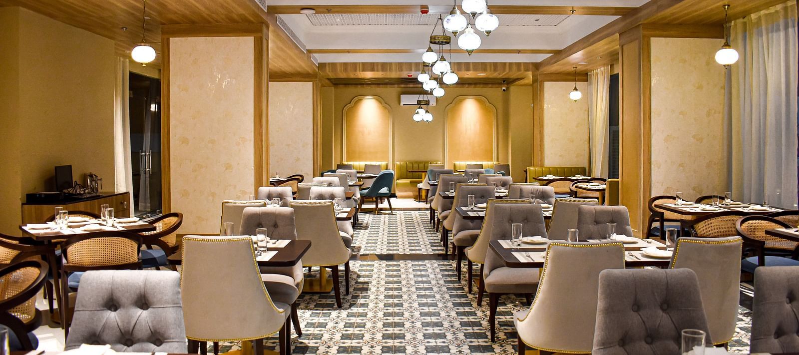 A restaurant interior with patterned tile floor, upholstered chairs, set tables, hanging pendant lights, and decorative ceiling panels - Urban Suites by BluSalzz, Jaipur