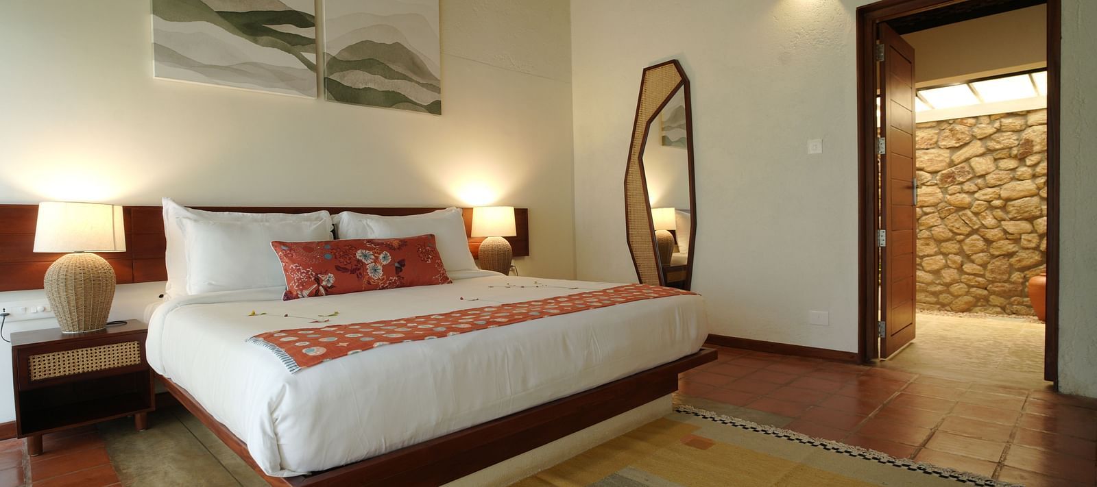  A well-appointed bedroom at Vaasta Vagamon featuring a large bed, bedside tables with lamps, a floor-length mirror, and artwork.