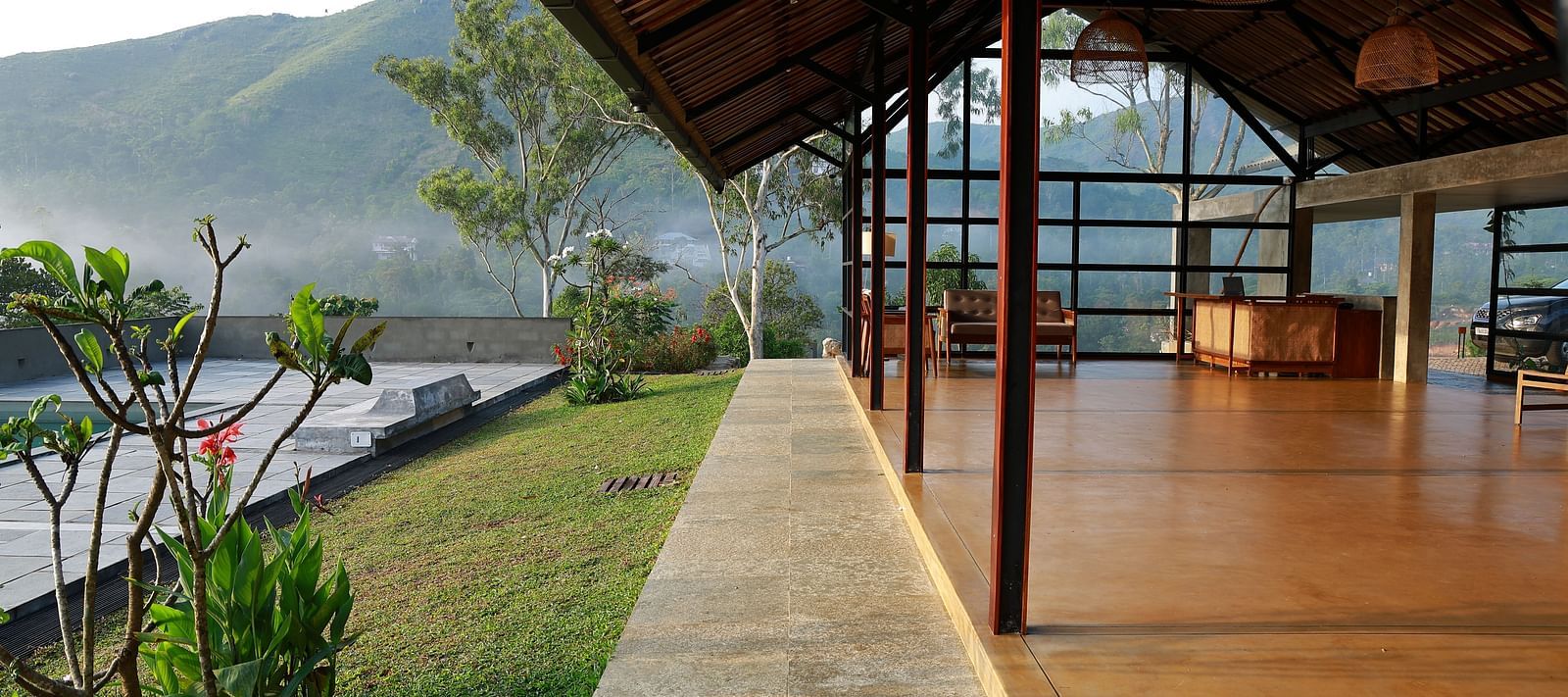  A spacious open-air pavilion at Vaastha Vagamon, featuring an exposed roof structure and offering panoramic views of the surrounding hills.