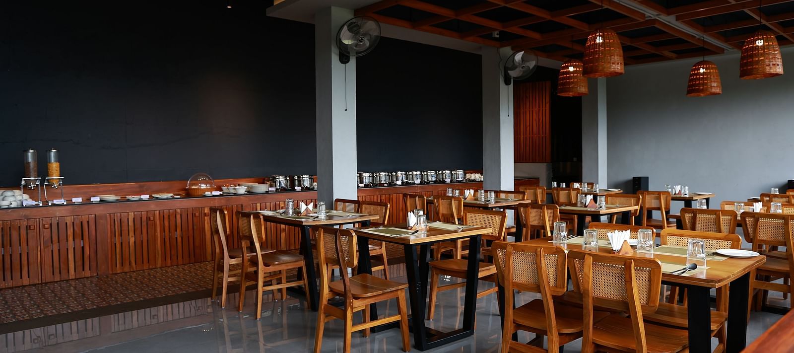  A well-appointed dining area at Vaastha Vagamon, featuring numerous tables and chairs, a buffet spread, and modern lighting fixtures.
