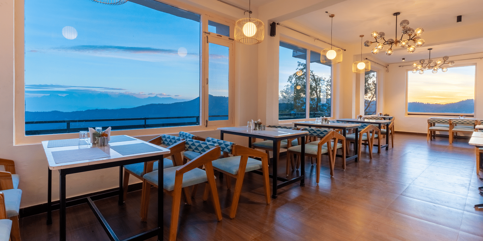 A close-up of a neatly set dining table positioned in front of a large window with scenic views at Himalayas Resort By The Lake Hill, Mukteshwar.