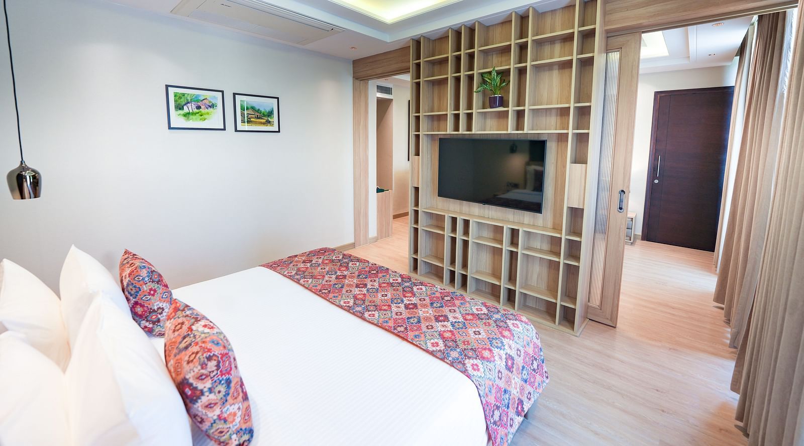 A bed in our suite featuring a floral-patterned bed runner and pillows, positioned in front of a wall-mounted television - NAMAMI BY ZENQ BANKHANDI
