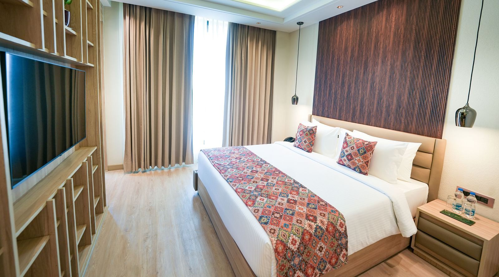An image of a queen size bed adorned with a floral-patterned bed runner, positioned in front of a wall-mounted television - NAMAMI BY ZENQ BANKHANDI