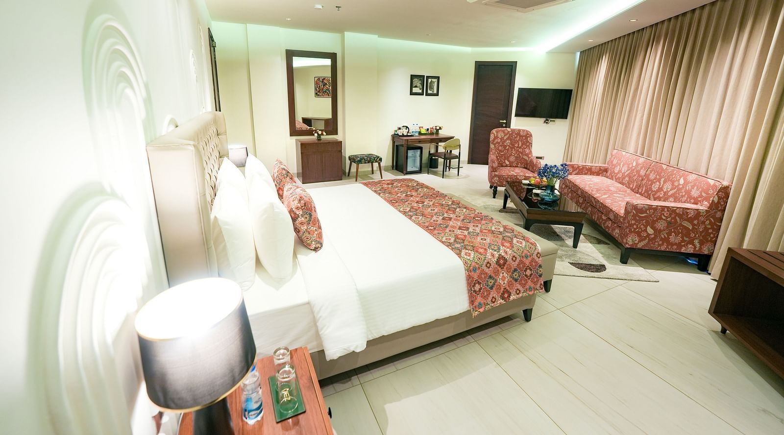 An image of our suite in Kangra with a queen size bed, upholstered furniture, and a wall-mounted mirror - NAMAMI BY ZENQ BANKHANDI