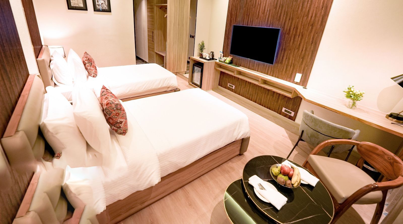 A hotel room with twin beds, a wall-mounted television, a coffee table and a cushioned chair - NAMAMI BY ZENQ BANKHANDI