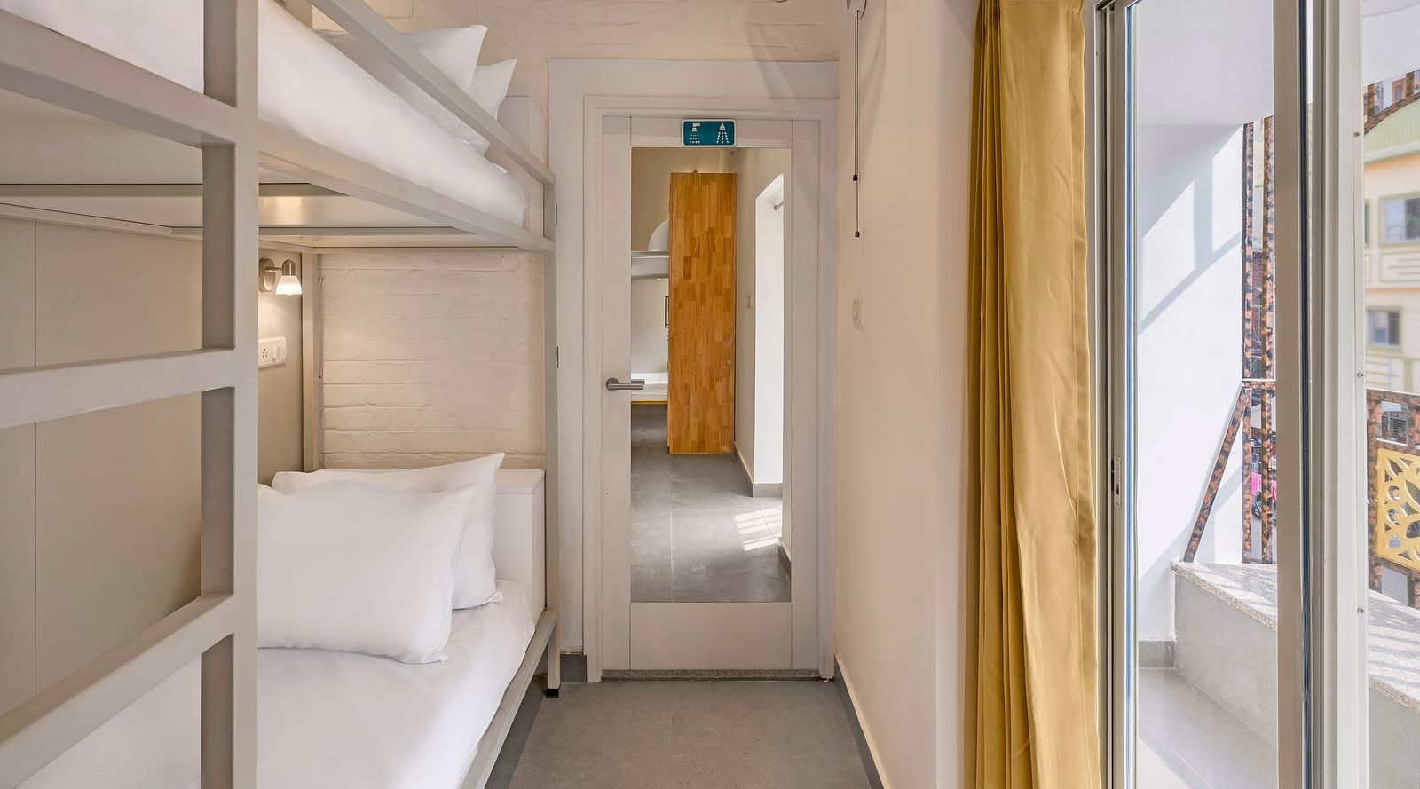 A front angle view of the dorms at Bedzzz in Varanasi showcases large windows adorned with curtains, inviting natural light into the space. The design combines comfort and functionality, creating a welcoming atmosphere for guests.