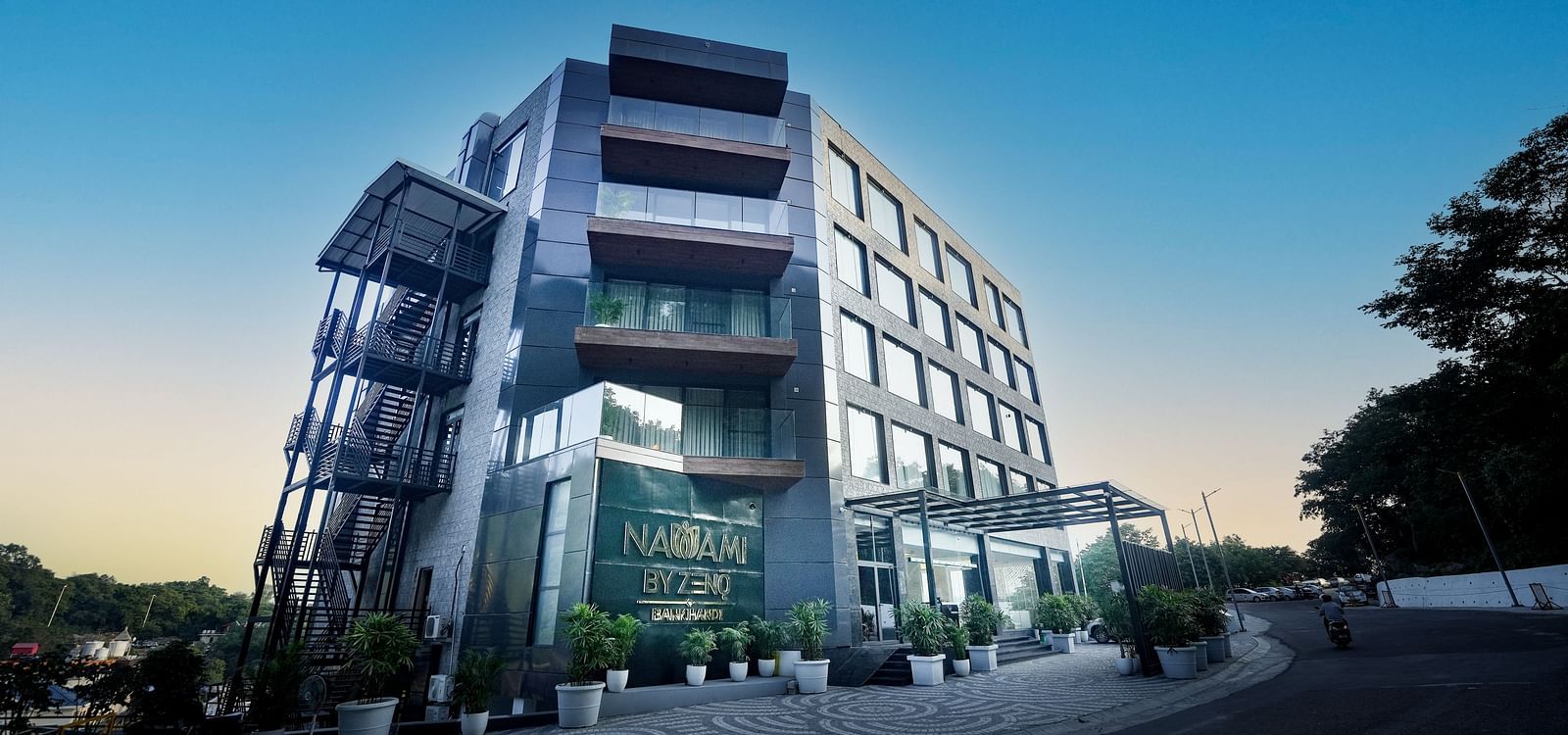 A twilight scene featuring a hotel structure with expansive windows and a sign displaying the name of the hotel - NAMAMI BY ZENQ BANKHANDI