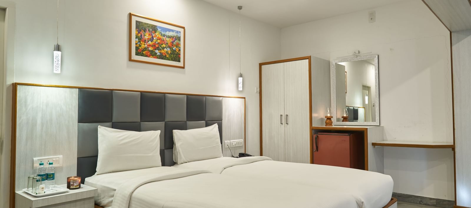 A comfortable and well-appointed hotel room at Hotel Mamallaa Heritage, featuring a large bed with crisp white linens, a bedside table, and wall-mounted art.