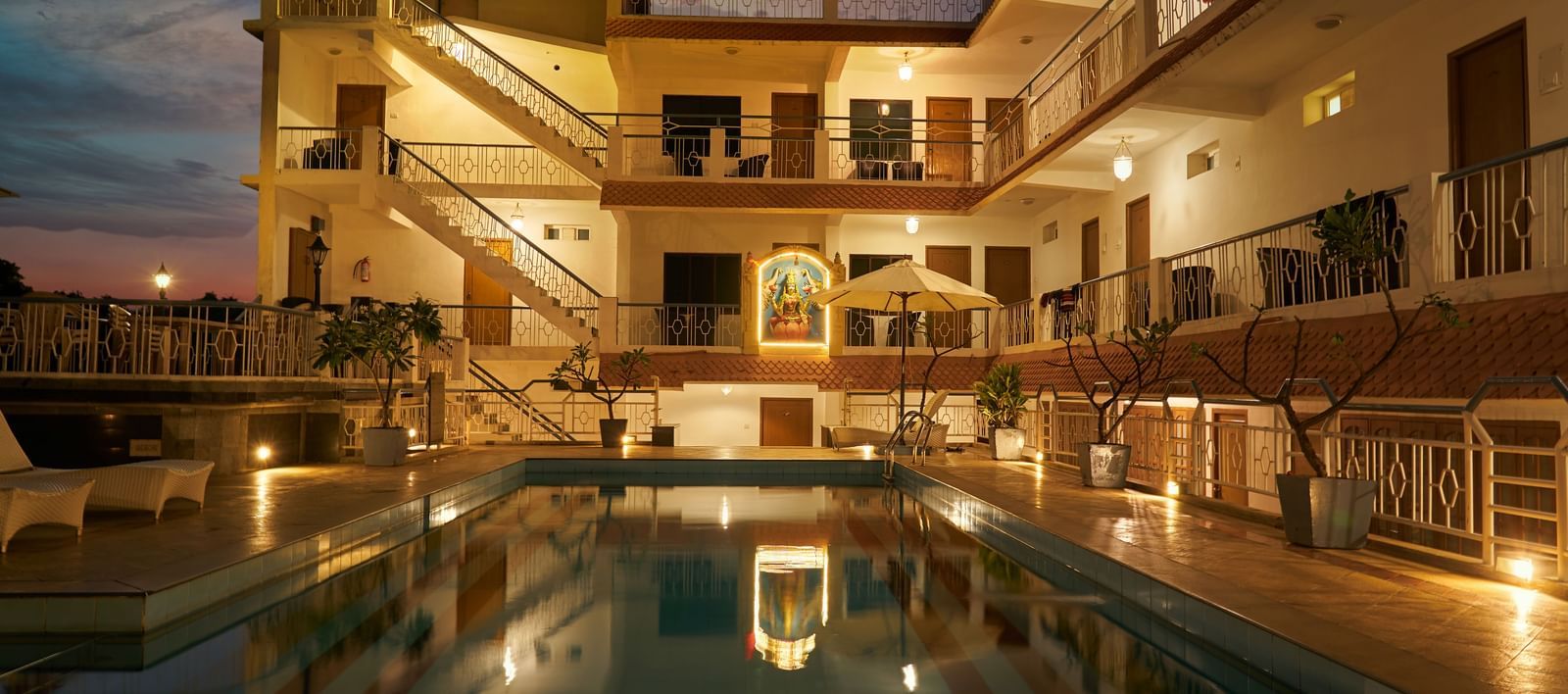 A nighttime view of Hotel Mamallaa Heritage, showcasing its illuminated facade and a beautifully lit swimming pool reflecting the lights.