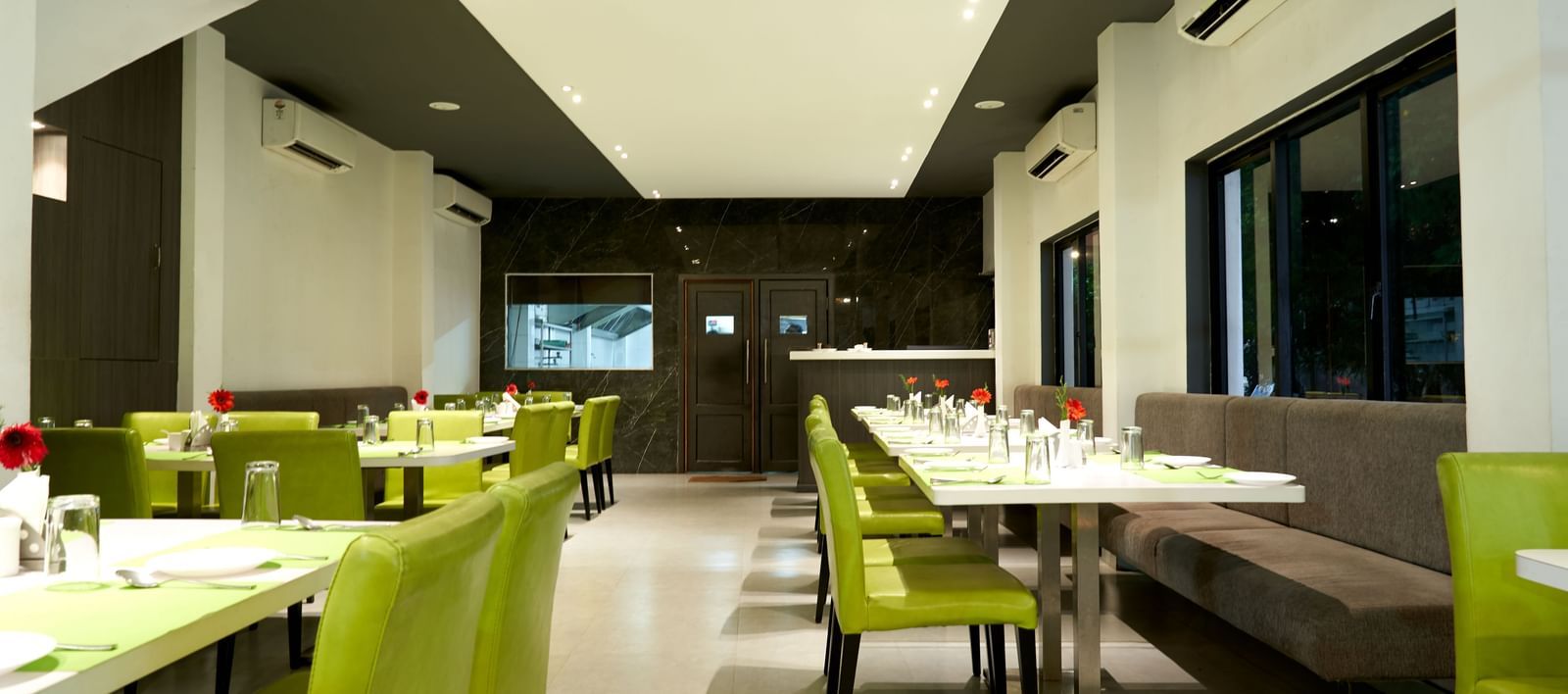 A modern restaurant interior at Hotel Mamallaa Heritage, characterized by bright lighting, white walls, and tables with vibrant lime green seating.