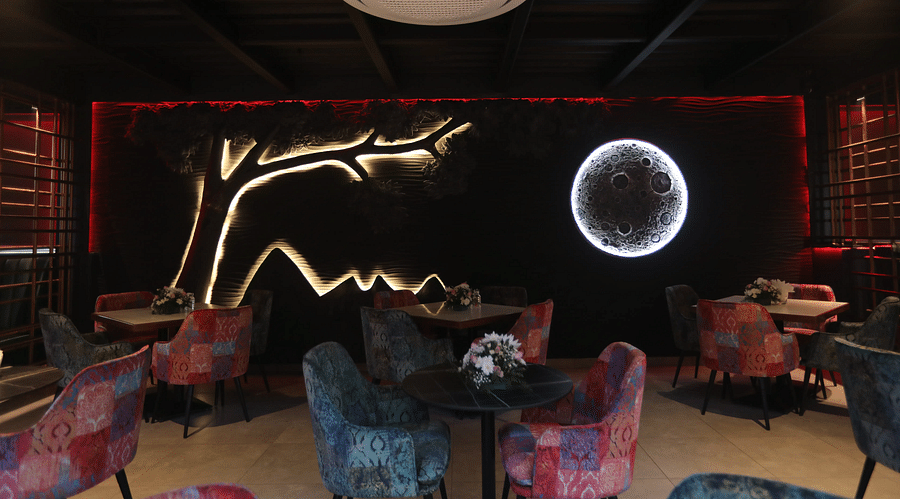 alt-text Vibrant dining area with patterned chairs and striking wall art of a tree and glowing moon, creating a cosy ambience - Nysa Skybar