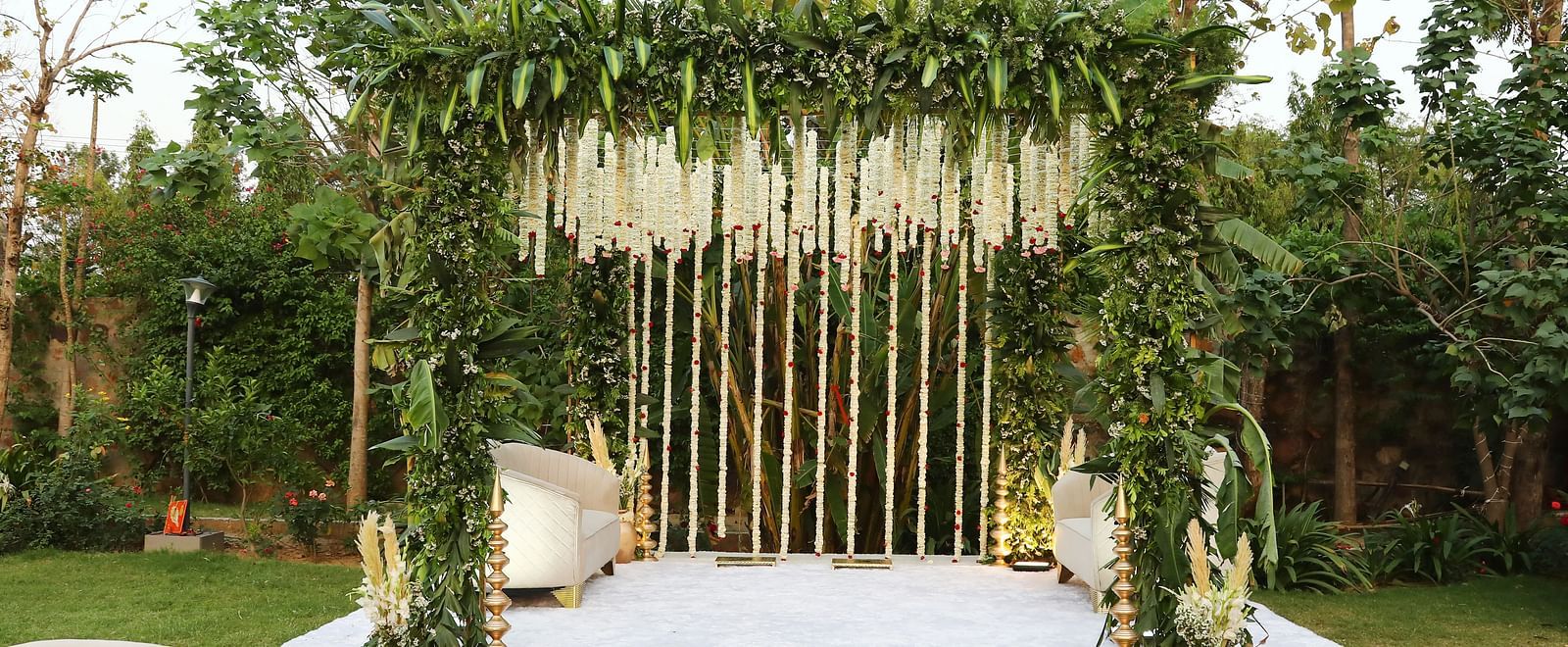 Floral wedding stage at Tisya Farms, Gurgaon with a white and green vertical decor and white seating.