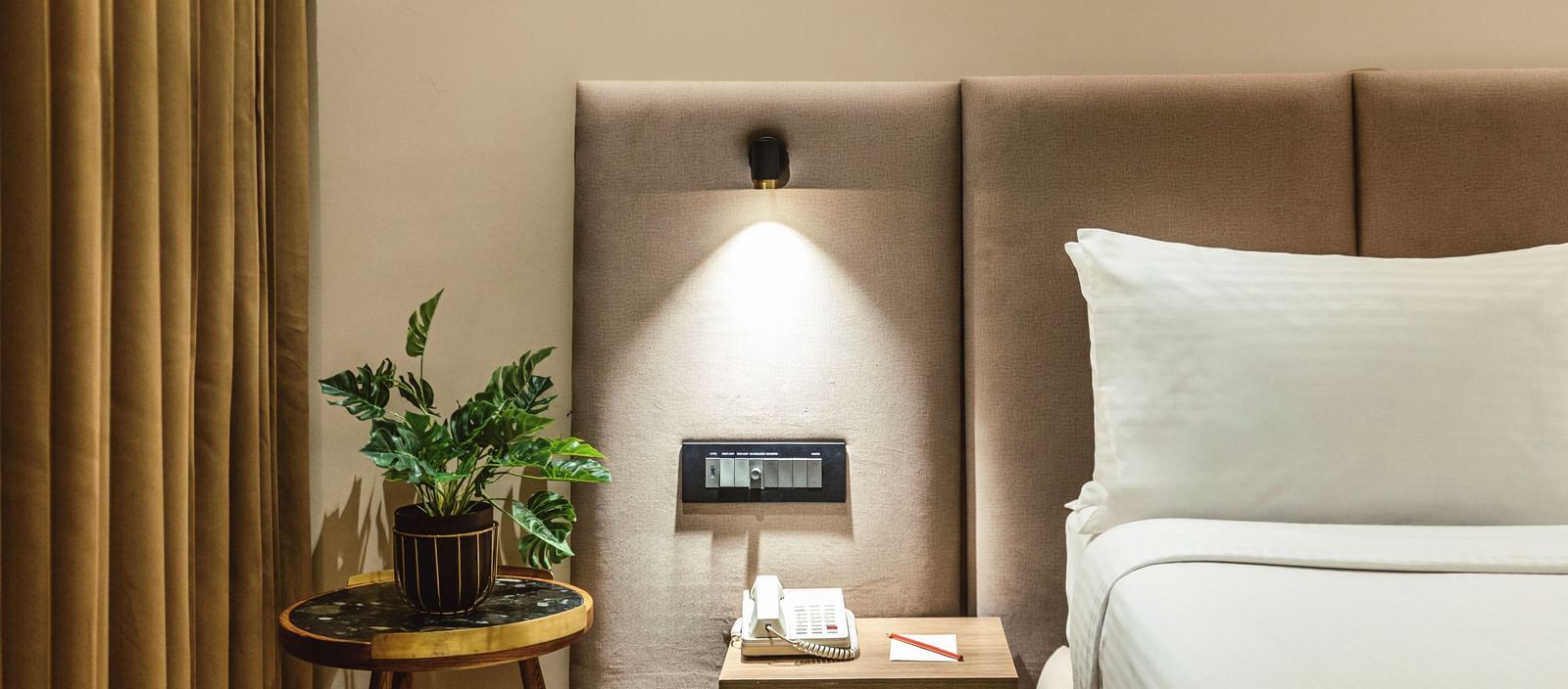 A close-up of a bed with a plant on a bedside table in a room at Mango Hill Central, Chennai.