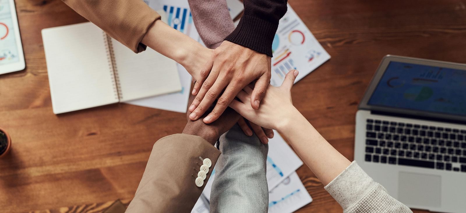Team members joining hands over a work desk, symbolising unity and collaboration.