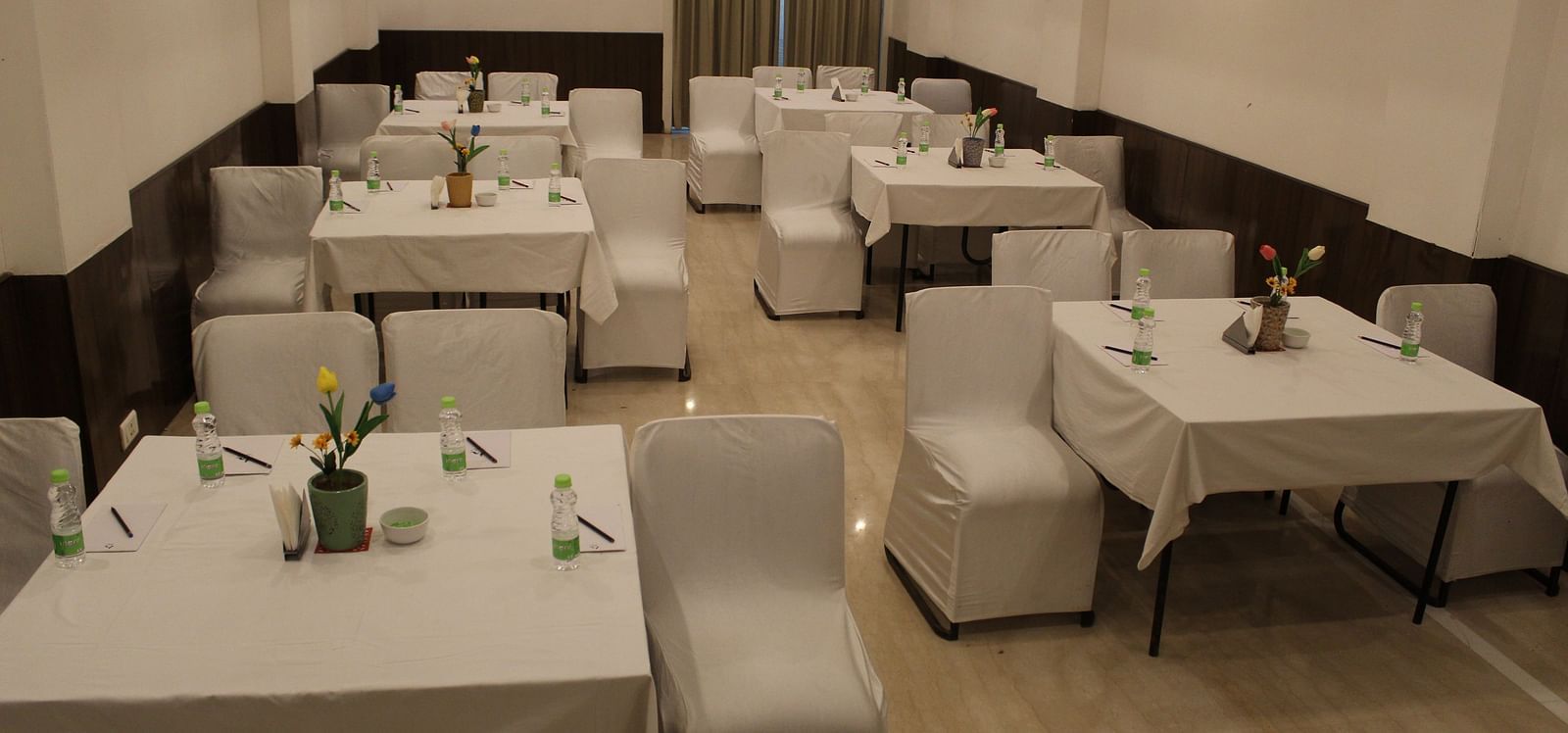 An image of a banquet hall at Inde Hotel Vista Woods featuring a few sets of tables with four chairs each