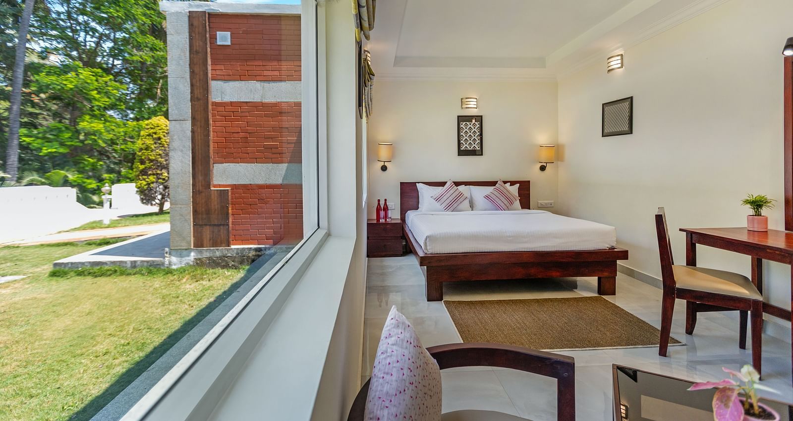 A bright hotel room with a bed, seen through a large window overlooking a garden with palm trees - Mango Hill Resort, Coimbatore