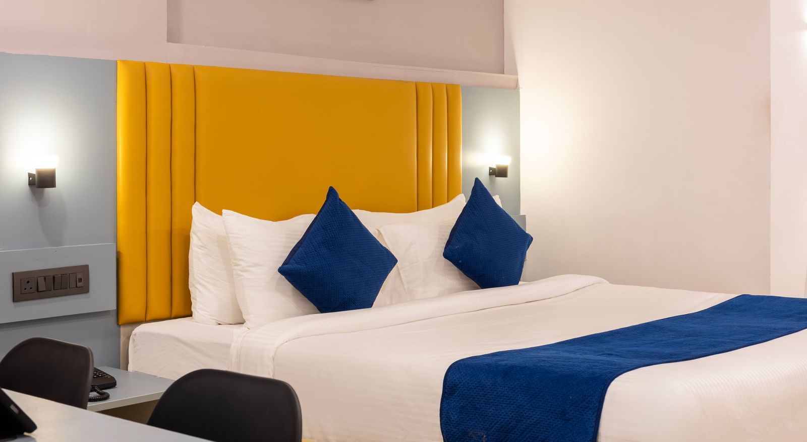 Close up side view of a modern Premium Room with a bed featuring blue accents, a work desk area, and a door on the left  - Beestay Hotels Financial District, Hyderabad 