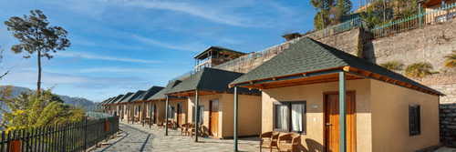 An image of cottage rooms from outside featuring a concrete yard at front and the entire villa is surrounded by trees in the hills - Suryavillas Luxury Resort and Spa, Solan