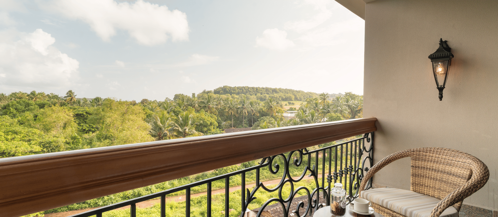 An expansive balcony with 2 arm chairs and a coffee table overlooking at the lush green lawn from the Classic Room (Diwa) at The Evren, Vagator.