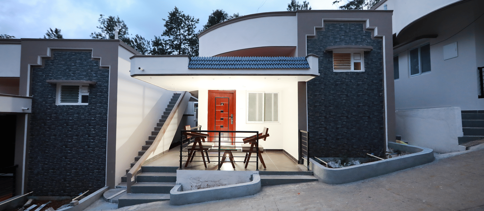 Front-view shot of the Nature Luxury Room exterior with the outdoor seating area lit up along with a cloudy sky in the background at WOW Naturefull Resorts, Yercaud.