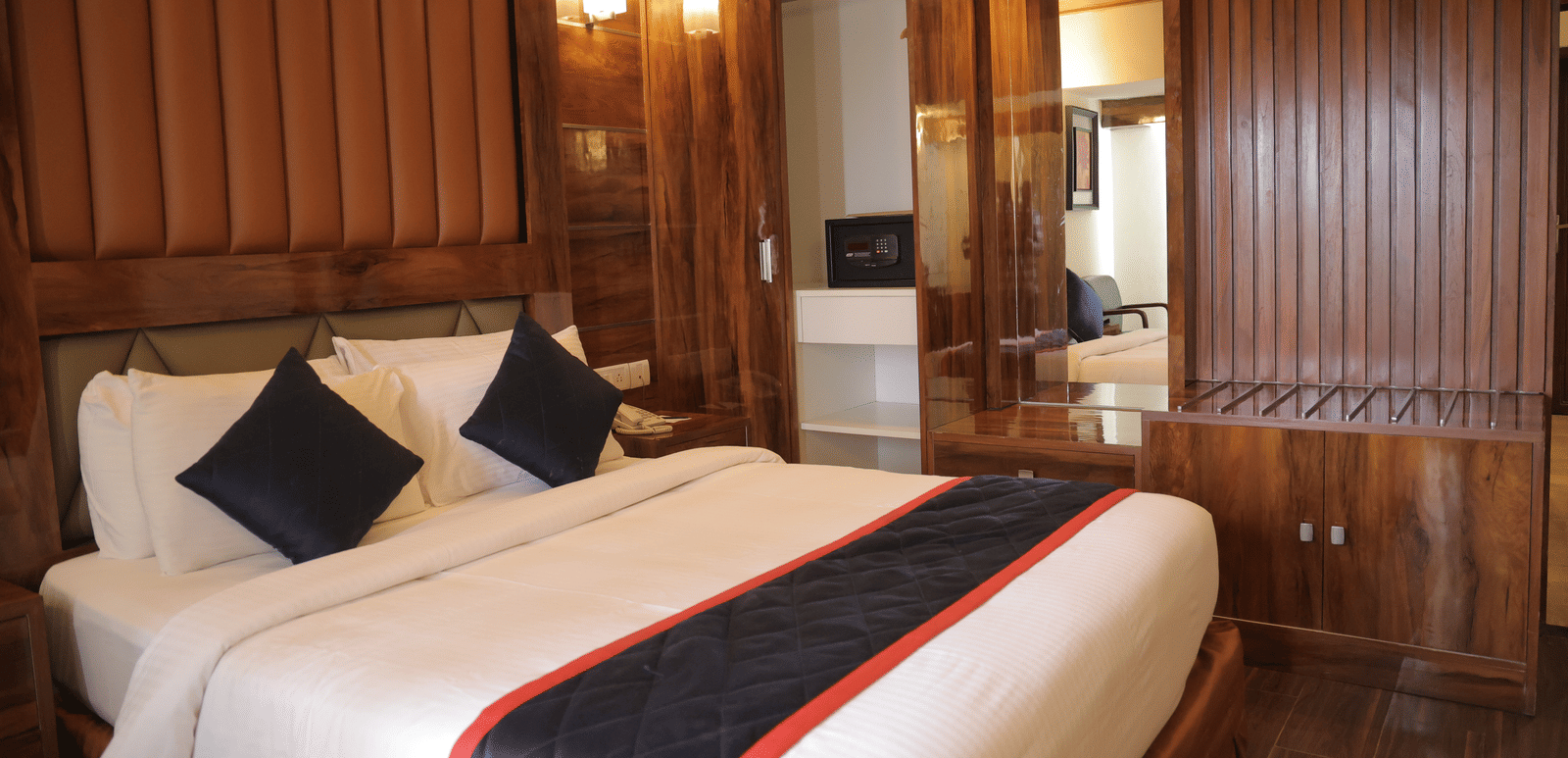 A spacious hotel suite with a large double bed, wooden panelling, and mirrored wardrobe doors - Benzz Park, Kodaikanal
