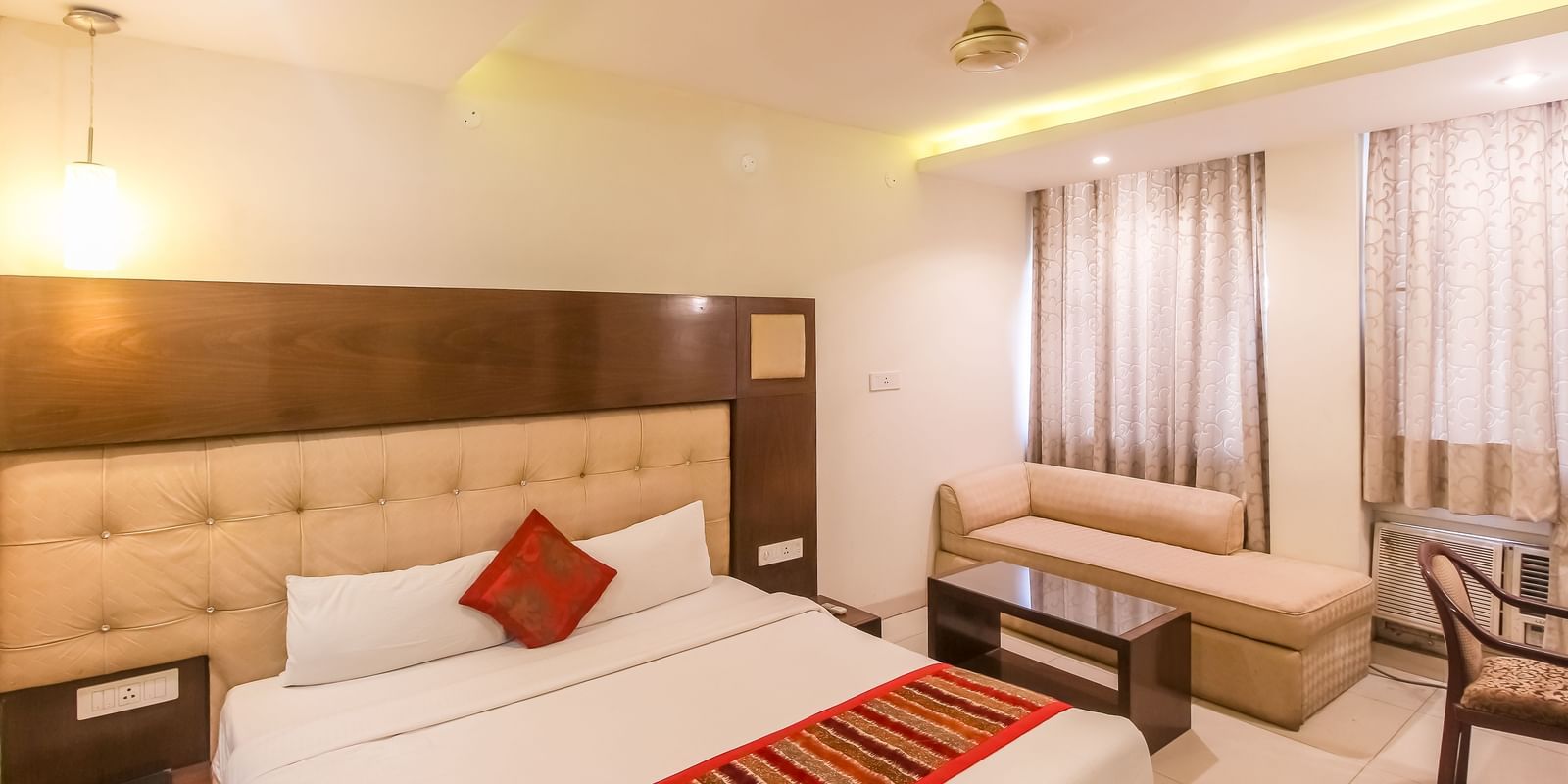 A cosy hotel room with a plush bed, a small sofa, and a glass-topped table. - Hotel Diamond Plaza, Chandigarh.