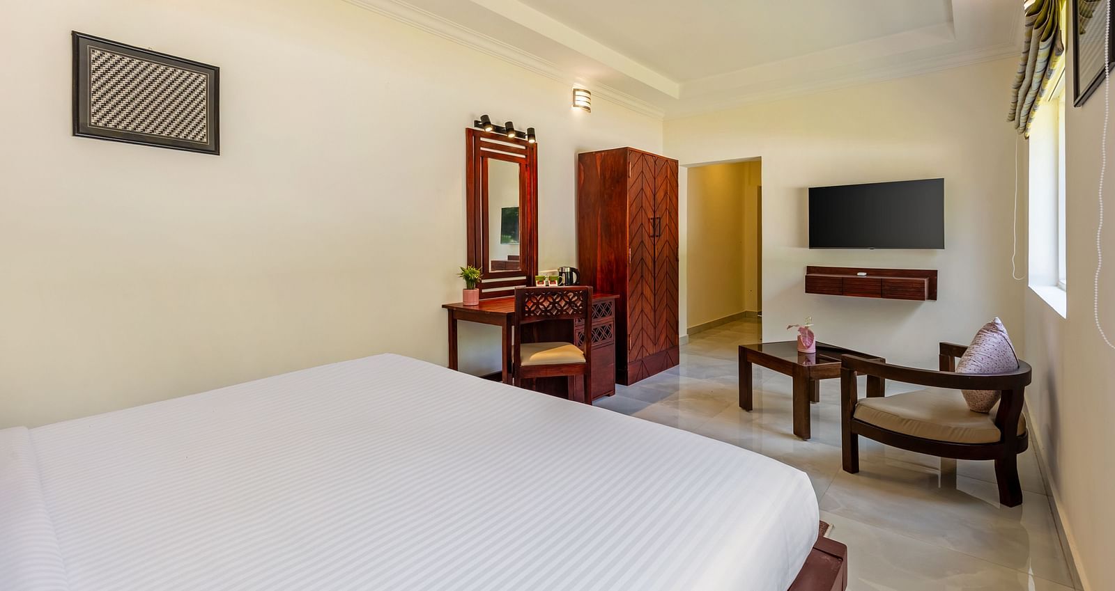 A well-lit hotel room with a bed, a desk, a wardrobe, a television, and a seating area - Mango Hill Resort, Coimbatore