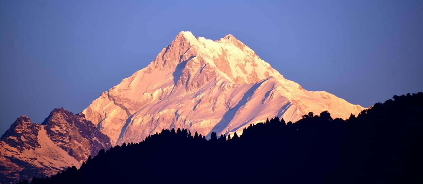 Snow-capped peak glowing in golden sunlight against a clear blue sky