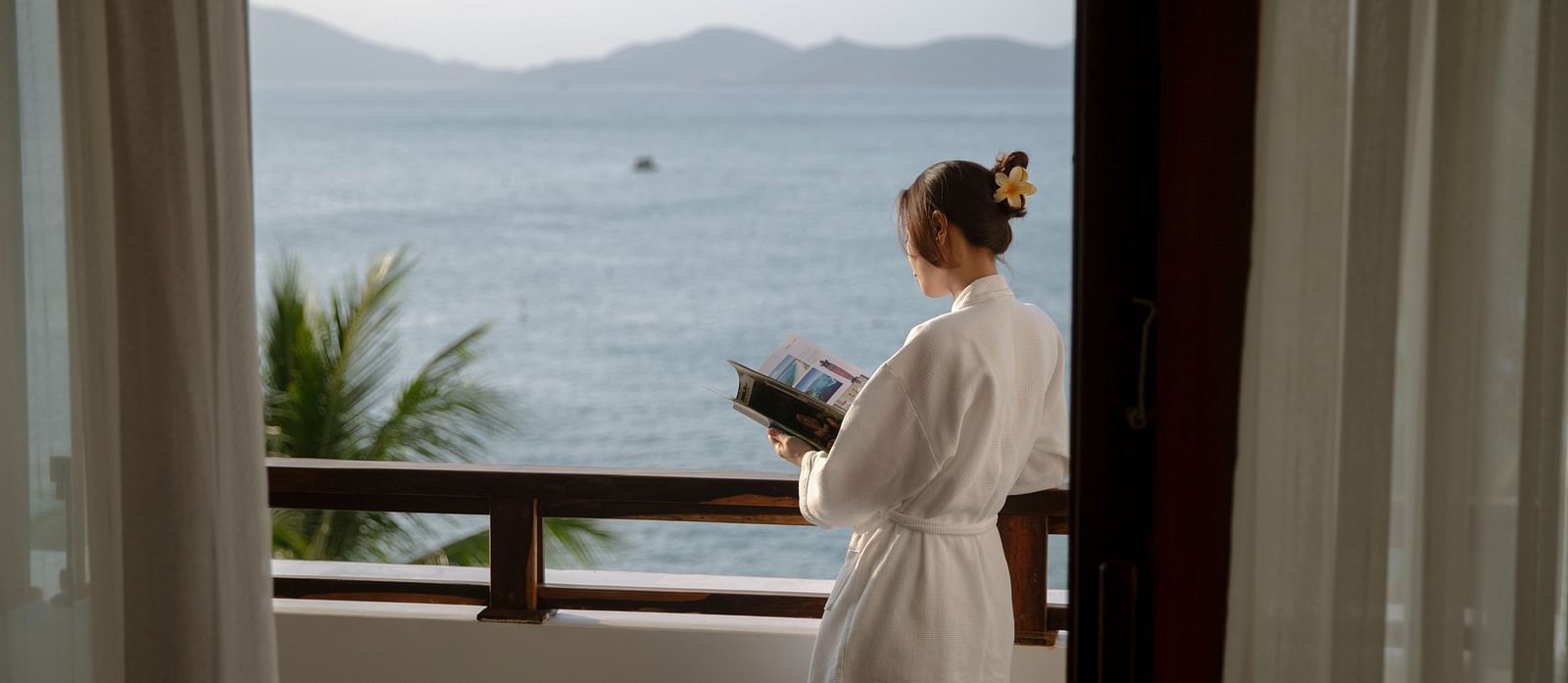 An image of a woman standing on the balcony An image of a huge sitting area of with several chairs and centre tables - Alibu Resort Nha Thrang