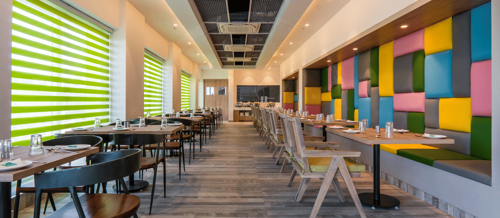 Full view of the dining area featuring a wooden floor along with colourful cushioned panels mounted on the wall at Hotel Le Roi, Dehradun.