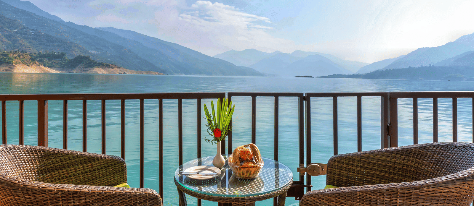 A closeup of two chairs surrounding a coffee table with the expansive views of the lake surrounded with mountain ranges at Le ROI Floating Huts & Eco Rooms.