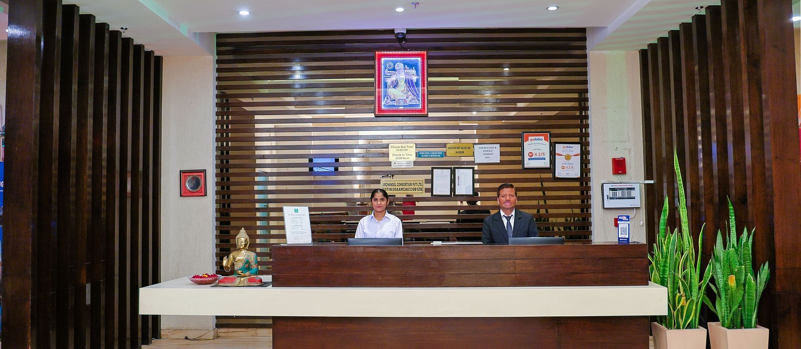 A wide wooden desk at the Le ROI Udaipur Hotel, where a female and a male staff member warmly greet the guests