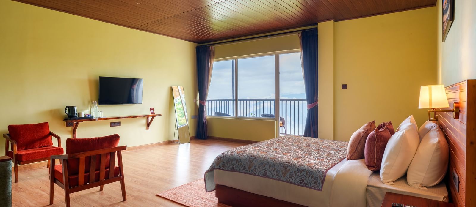 Bright bedroom with a double bed, TV, seating area, and large windows offering natural light.