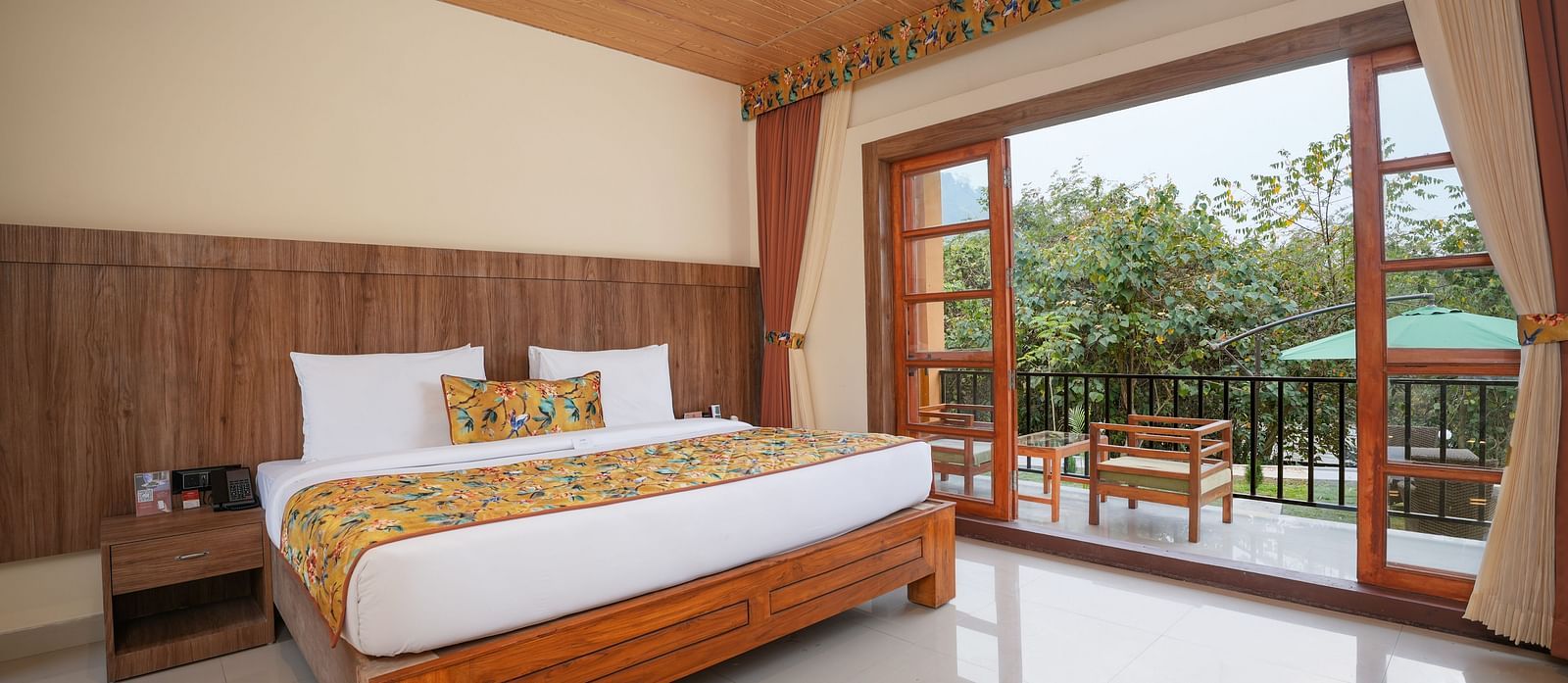 Bungalow featuring a spacious bed with wooden headboards, bedside table, and a large balcony at Summit Green Lake Tea Resort & Spa, Kaziranga