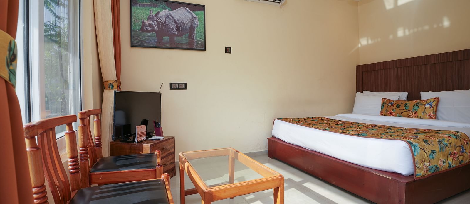Deluxe Cottage featuring a spacious bed, television, air conditioner, glass table, and chairs at Summit Green Lake Tea Resort & Spa, Kaziranga
