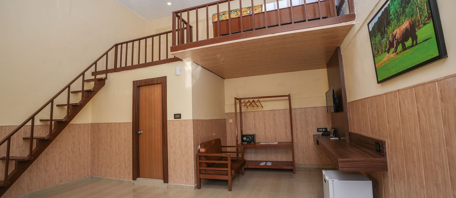 Duplex room with balcony features a living area with wooden furniture, a wine fridge, wall-mounted television, and stairs leading to the spacious bedroom at Summit Green Lake Tea Resort & Spa, Kaziranga