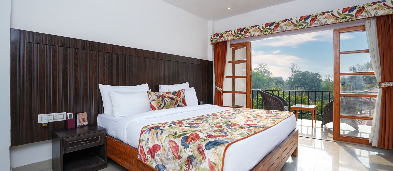 The suite with balcony offers a stunning nature view through large doors that open onto furniture and a glass table at Summit Green Lake Tea Resort & Spa, Kaziranga