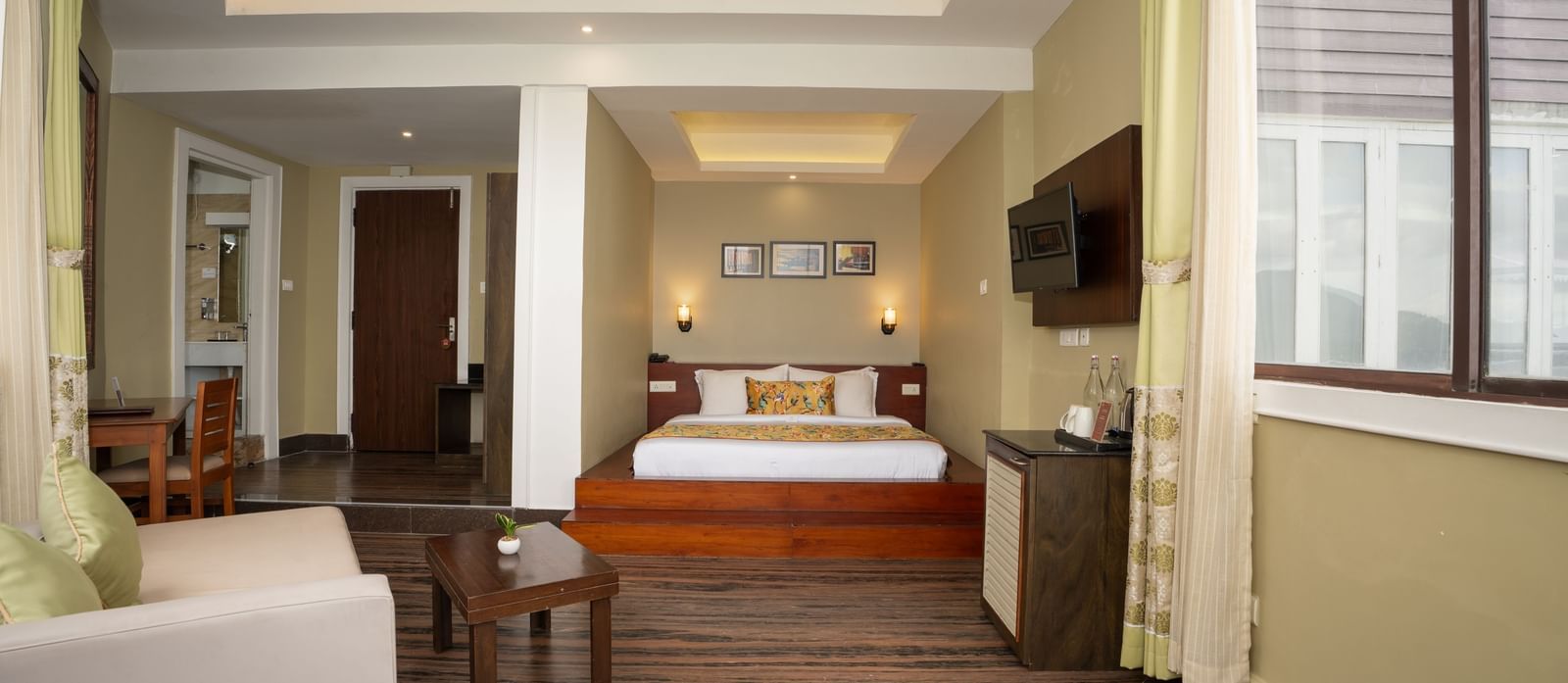 Honeymoon Suite with Valley View at Summit North Star, Gangtok featuring a bed in one coner, a cabinet table, flat TV screen on the wall, a sofa and a centre table.