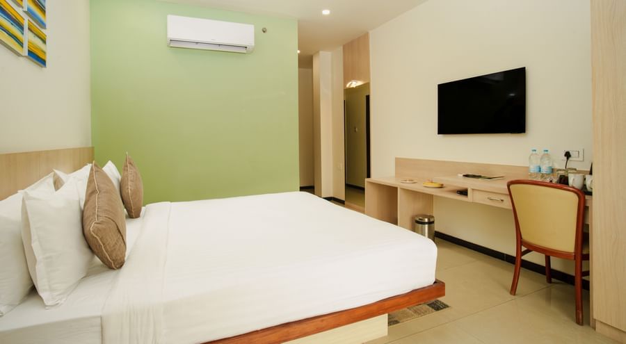 Hotel room with a large bed, desk, wall-mounted television, and a subtle green accent wall at Arawali Ananta Elite, Jaipur.