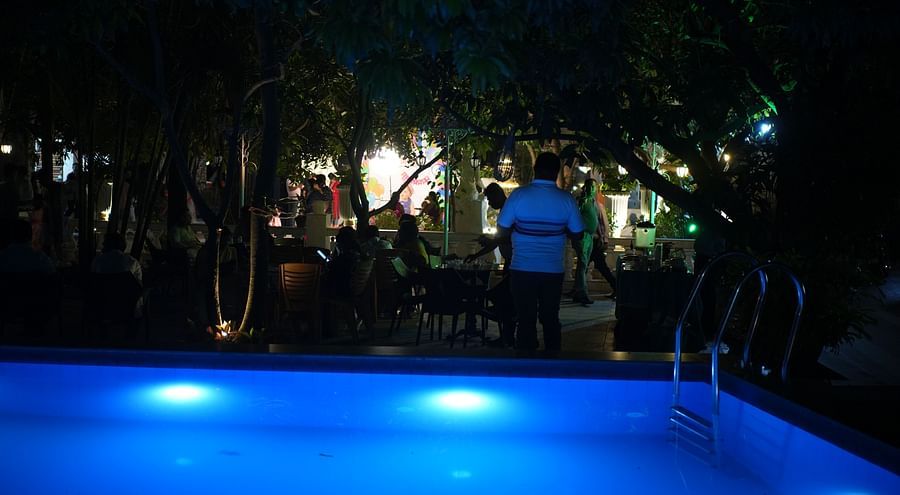 Night view of the swimming pool featuring the garden nearby with people roaming around at Rangamati Garden Resort.