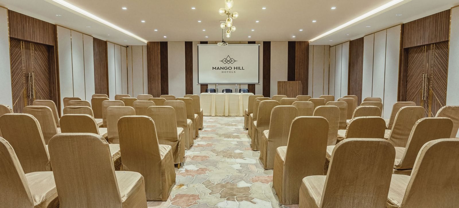 Banquet hall at Mango Hill Central, Chennai, with chairs arranged in rows facing a screen and a table at the front. The room is set up in a theatre style.