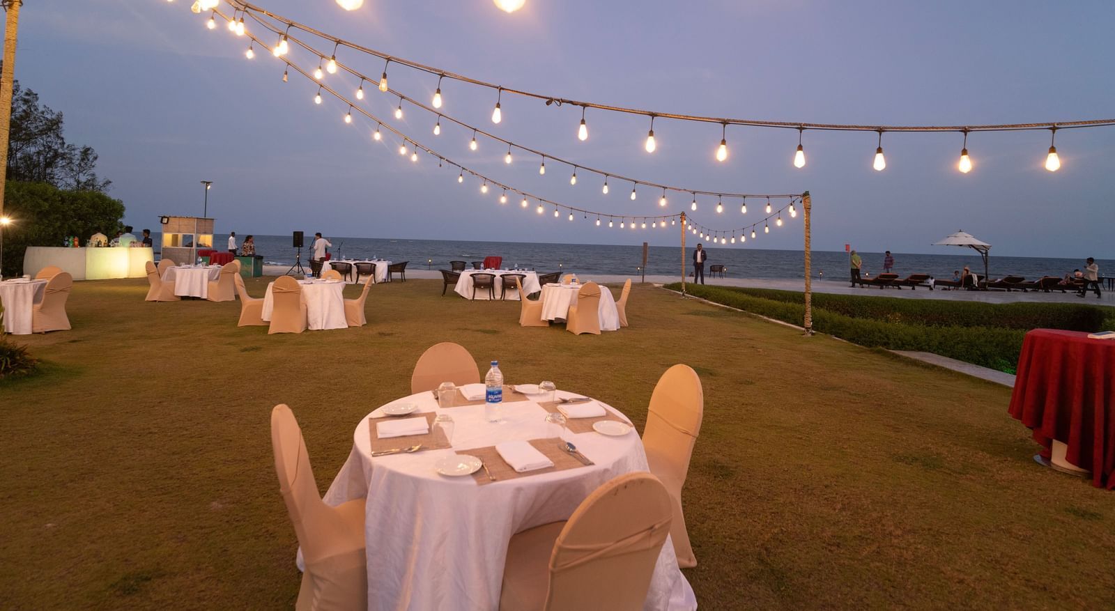 Round tables with white chairs set up on a lawn under string lights - Kaldan Samudra Palace