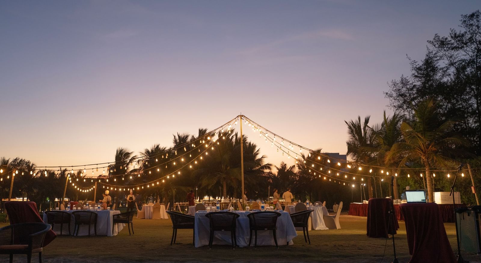 Outdoor evening event setup with string lights and a sunset backdrop - Kaldan Samudra Palace